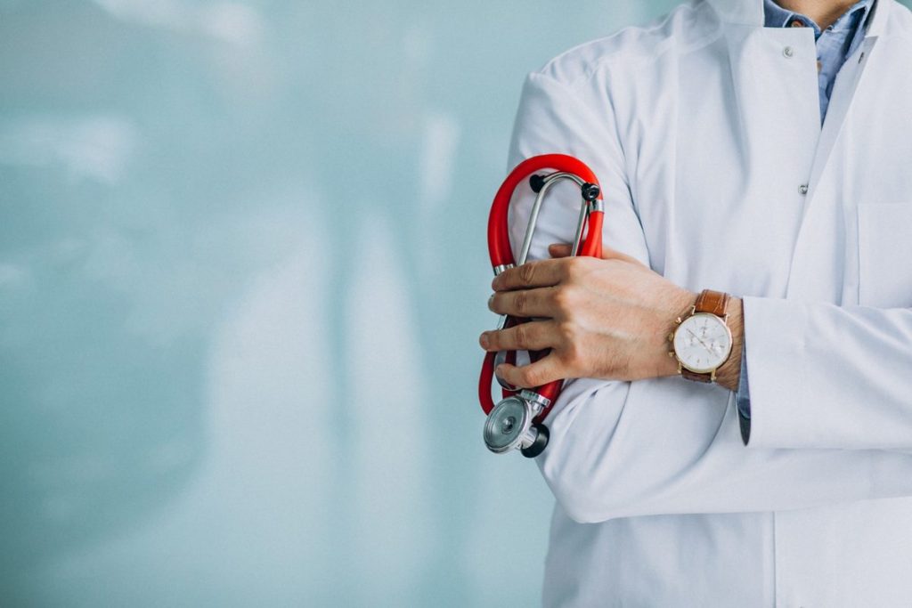 Médico de jaleco branco segurando estetoscópio em ambiente clínico