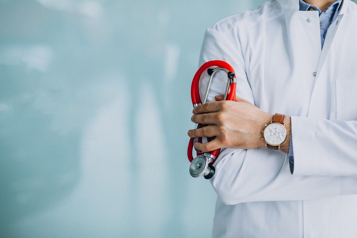 Médico de jaleco branco segurando estetoscópio em ambiente clínico